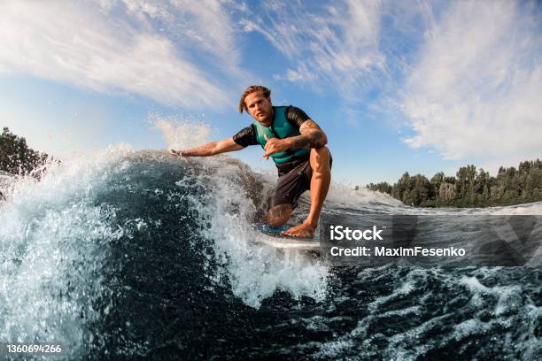 Athletic Guy Wakesurfer Skilfully Riding Down The Blue Splashing Wave On A Warm Day Stock Photo - Download Image Now