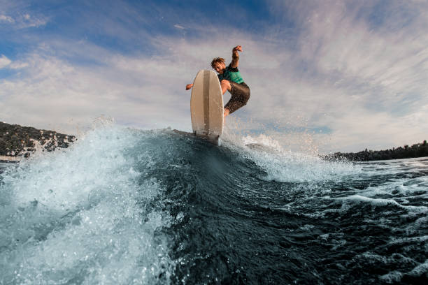 istock Active male wakesurfer jumping on a wake board on splashing river wave against sky 1360694425