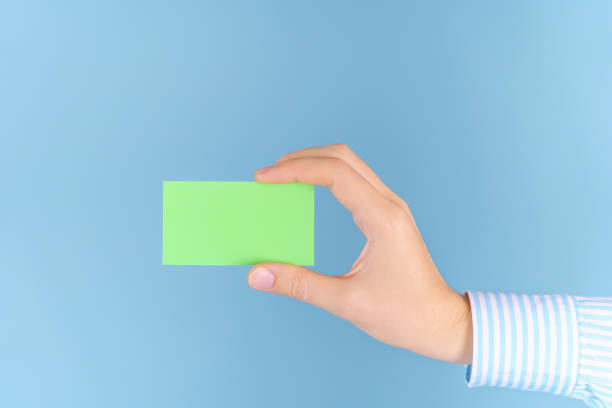istock A woman's hand holds a green empty business card on a blue background, a mockup 1360695393