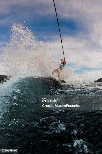 View Of Great Splashing Wave And Man Holds Rope And Glides On The Waves On The Wakesurf Board Stock Photo - Download Image Now