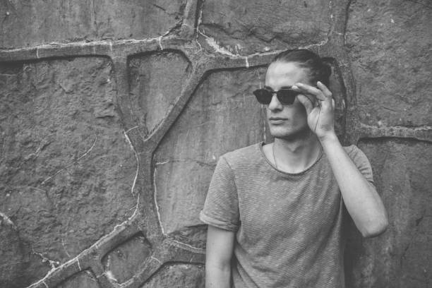 istock Young transsexual man with sunglasses posing in front of stone wall 1360696090