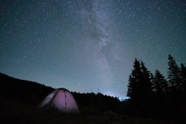 istock Bright illuminated tourist tent glowing on camping site in dark mountains under night sky with sparkling stars. Active lifestyle concept. 1360696462