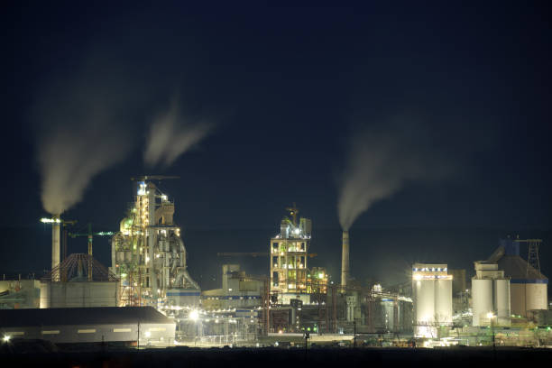 istock Illuminated cement plant with high factory structure and tower cranes at industrial production area at night. Manufacture and global industry concept 1360696471