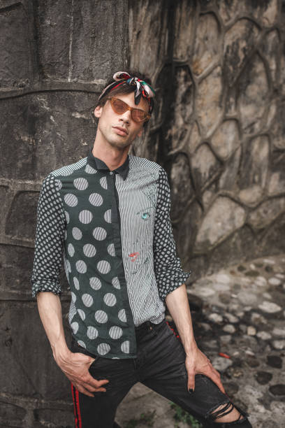 istock Young transsexual man with sunglasses posing in front of stone wall 1360697178