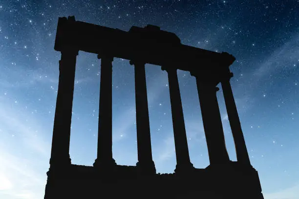 A silhouette of the Temple of Saturn in the Roman Forum on a starry night.