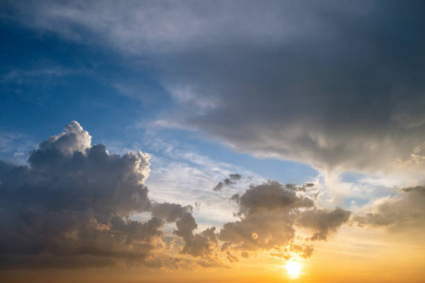 istock Dramatic yellow sunset landscape with puffy clouds lit by orange setting sun and blue sky. 1360698207