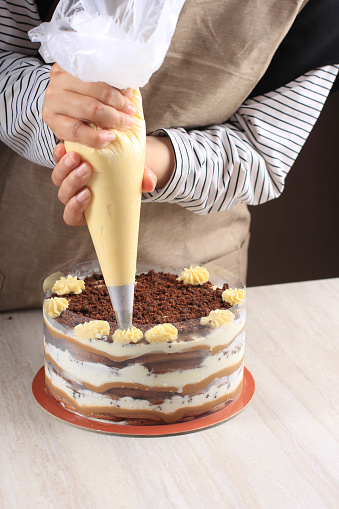 Confectioner at Work. Cream Cake Decorating. Cook Table Preparing a Tiramisu Cake on a Brown Background.