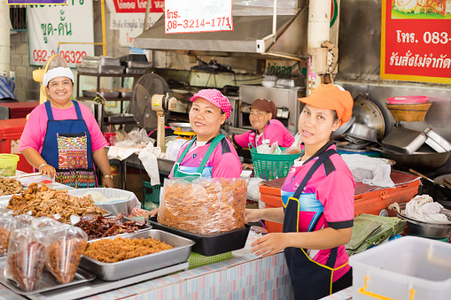 Small group of cooking thai vendor women on local market in province of Sukhothai. Women are standing in cooking area with several cooked food