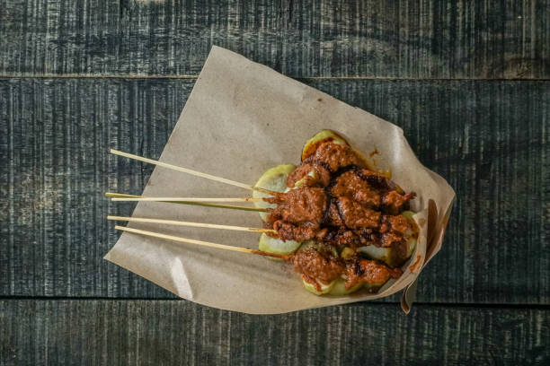 One serving of chicken satay with food paper wrap on a black painted wooden table. Chicken satay is a typical food from Madura Province, Indonesia
