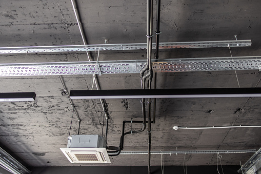 Air conditioner cassette and metal pipes and lightning on concreate ceiling in industrial building