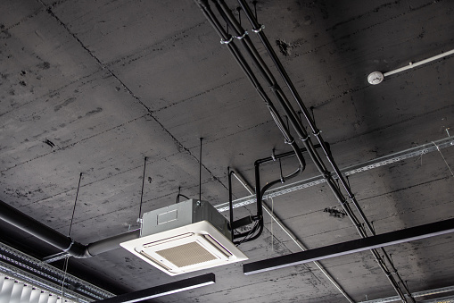 Air conditioner cassette and metal pipes and lightning on concreate ceiling in industrial building