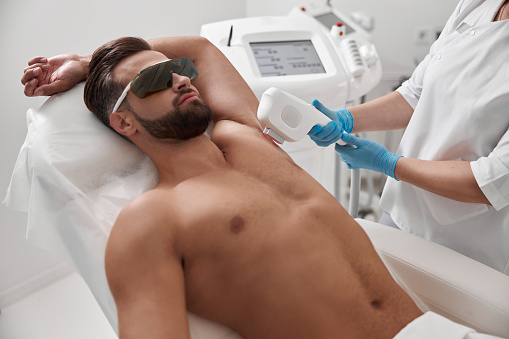 Hombre con gafas y pecho desnudo se somete a un procedimiento de depilación láser en la axila en la clínica photo