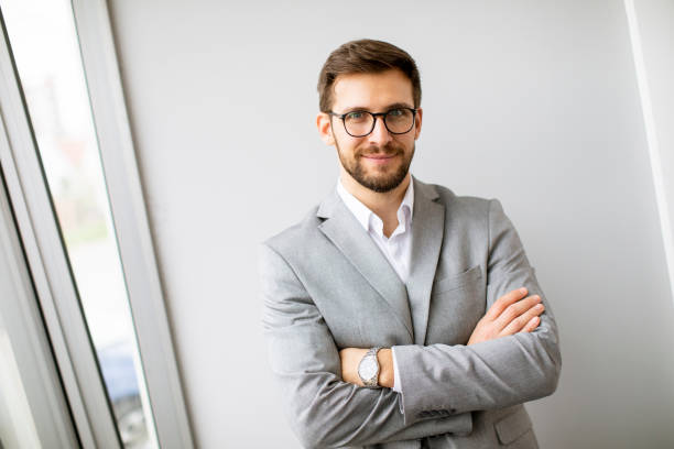istock Young modern businessman standing by the wall in the office 1360719104
