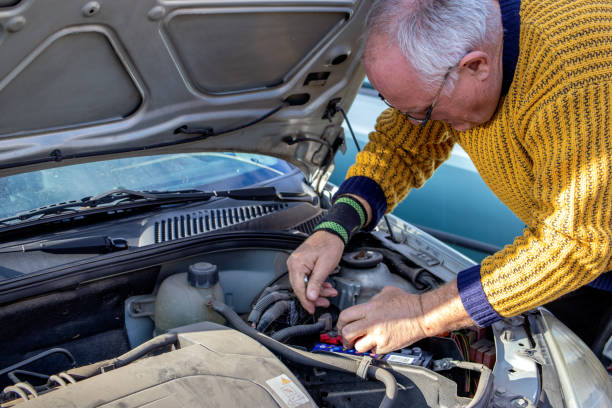 старший механик проверяет и меняет автомобильный аккумулятор. - old men car oil стоковые фото и изображения