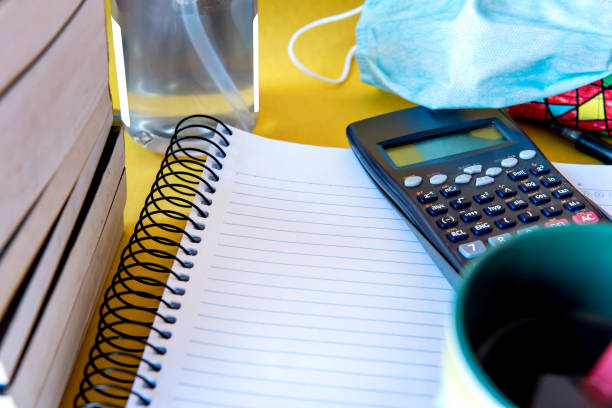 istock Messy table with notebook, calculator and books. Education, alcohol gel and mask, prevention for COVID-19. 1360730723