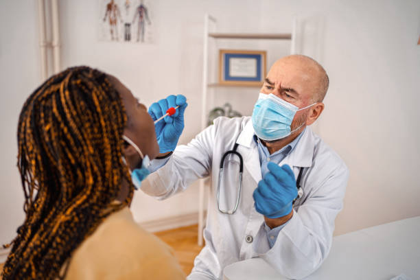 istock Doctor testing black female patient on possible coronavirus infection by taking a swab from mouth 1360731931