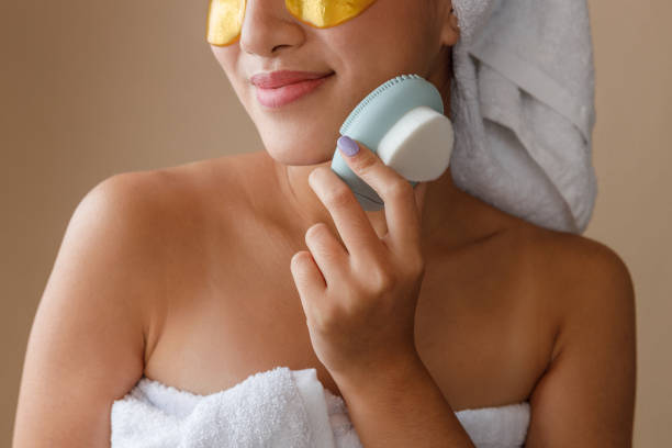istock Smiling young woman using face massager after shower 1360735253