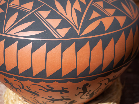Close up of a Native American painted terracotta pot with geometric patterns and leaf and lizard decorations in black.