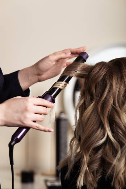 manos femeninas de un maestro del cabello. primer plano del cabello rubio en un rizador. curling curling curling. - probador establecimiento comercial fotografías e imágenes de stock