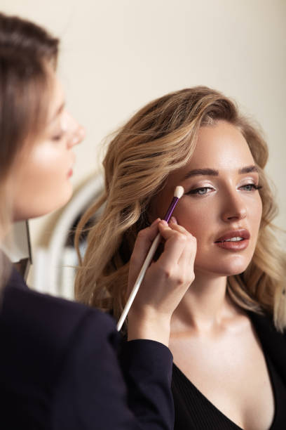 Portrait of lovely blonde model wearing professional make-up. Applying shadows. Makeup artist at work. Portrait of lovely blonde model wearing professional make-up. Applying shadows. Makeup artist at work. makeup artist stock pictures, royalty-free photos & images
