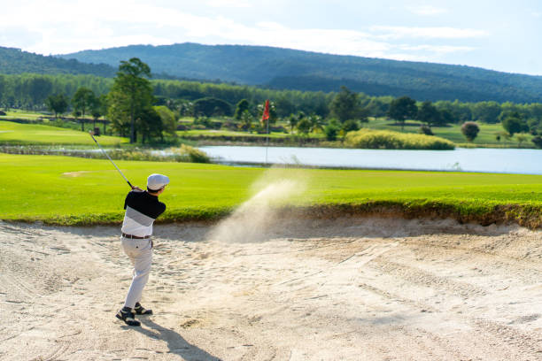 homem asiático batendo bola de golfe de um bunker para o verde no campo de golfe - golf swing golf teeing off men - fotografias e filmes do acervo