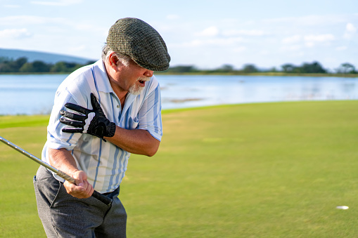 Asian senior man caught injury shoulder while golfing at country club on summer vacation. Elderly male golfer shoulder pain while outdoor sport workout. Senior people medical and healthy care concept