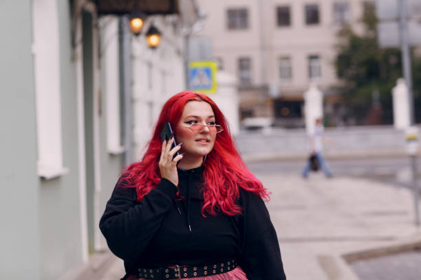 europäische plus-size-frauen verwenden mobiltelefon im freien. junge rotrosa haarkörper positive mädchen gehen auf der stadt straße im freien. - teen obesity stock-fotos und bilder