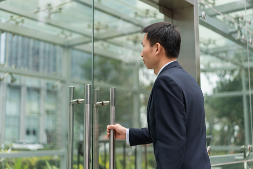 Asian male white-collar workers are preparing to open the glass door by hand