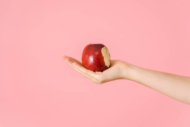 istock A bitten red apple in an open female palm on a pink background 1360780717