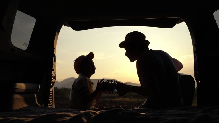 Asian father and son in back of car. Playing a guitar and relaxing in nature. Weekend travel.