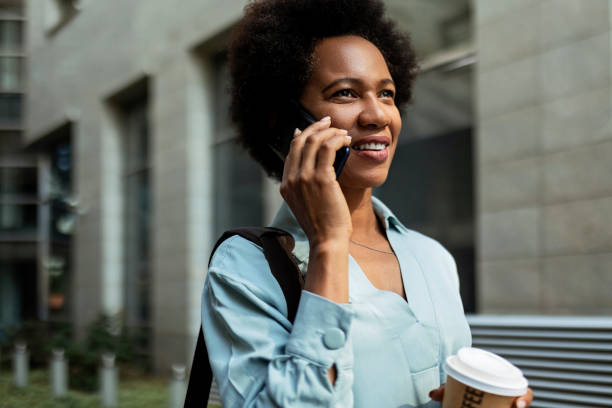 istock Young African-American woman using smart phone talking holding coffee cup 1360785946