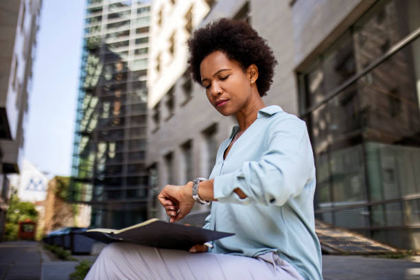 istock Young African American woman writing in a small notepad journal while looking at wristwatch 1360786589