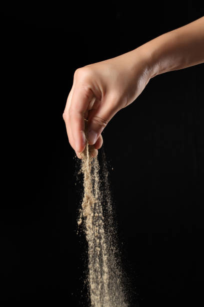istock Hand sprinkling ground pepper on black background 1360786623