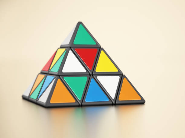 Pyramid shaped puzzle cube with colorful triangle shapes standing on yellow background stock photo