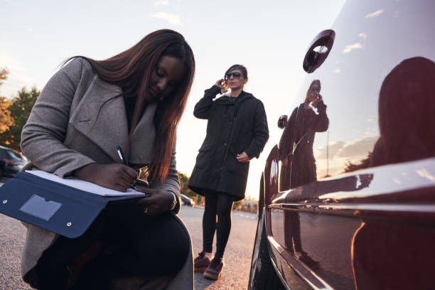 istock insurance agent examines the car while the driver talks on the mobile phone. Accident claim process. African-American woman checking the damage to the car after an accident. Concept of transportation. 1360795590