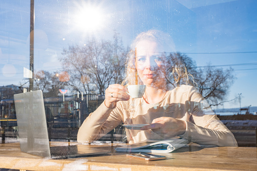 View through window of a young woman drinking coffee in coffee bar