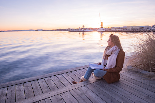 Young female reading a book and sitting on the pier