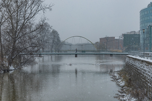 Wroclaw, Poland - December 3 2020: Footbridge over icy river at snowy winter with walking woman on it