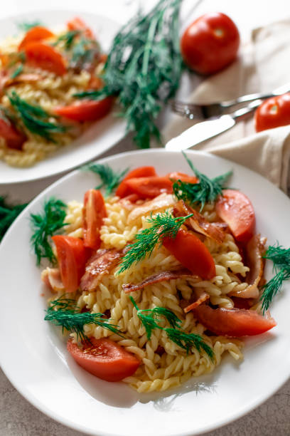 istock Pasta in carbonara sauce with fried bacon and fresh tomatoes, garnished with dill.  Appetizing hearty portions on the table, colorful dishes 1360802434