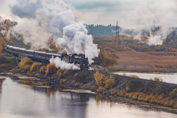 el tren de vapor retro se mueve a lo largo del lago en la mañana nublada de otoño. república de carelia. - railway bridge fotografías e imágenes de stock