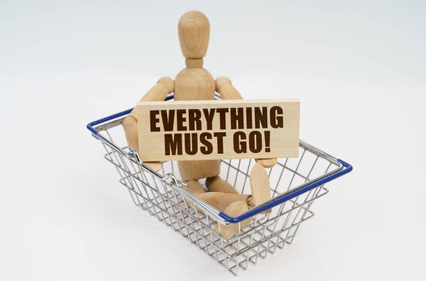 A wooden man sits in a shopping basket, holding a sign in his hands - Everything Must Go Business and finance concept. A wooden man sits in a shopping basket, holding a sign in his hands - Everything Must Go closing down sale stock pictures, royalty-free photos & images