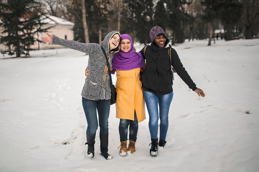 Portrait of three multiethnic female friends walking in the snow at the park