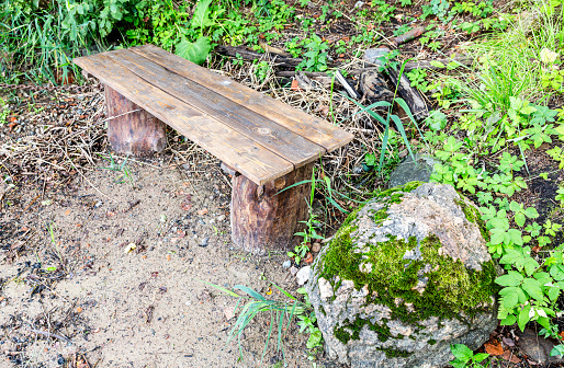 Handmade wooden bench and mossy stone on the bank of the lake in summer