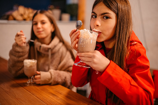Two little girls sitting at the table outside and drinking hot chocolate.