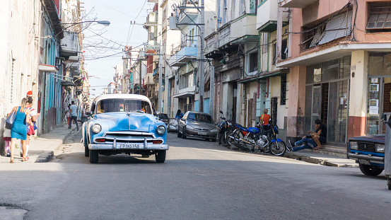 Havana, Cuba-December 2017: Authentic view and atmosphere on the streets of Havana. Cuban car driving true the neighbourhood filled up with local people and colonial residences in the background.