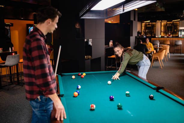 istock Young man enjoying while looking at his girlfriend playing billiard. In the background are the guests of the bar sitting at the table and drinking. 1360820523