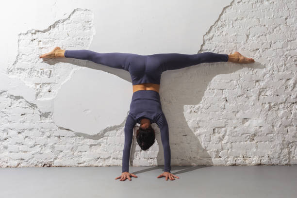 A woman trainer practicing yoga performs the Adho Mukha Vrikshasana exercise with Samakonasana, a handstand with a transverse twine leaning her body against the wall, inverted asana