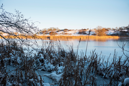 Landscape with a frozen lake, snow and golden, warm sunlight.