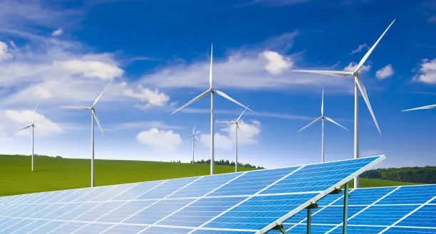 Solar panels with wind turbines against blue sky background