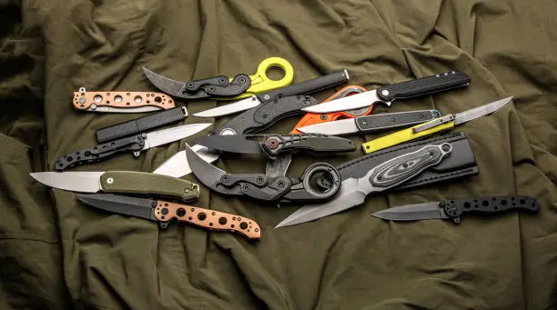 Photo of A variety of folding and pocket knives lie on khaki fabric. A versatile pocket tool and self-defense tool.